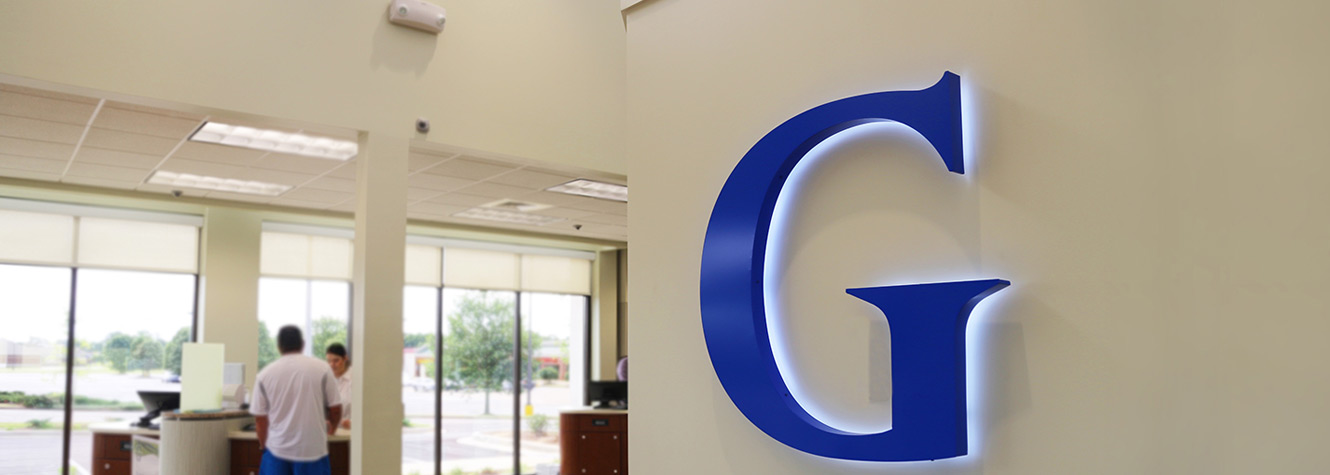 photo of the inside of a Guardian Branch, a large blue G is pictured on the wall with members conducting transactions in the background