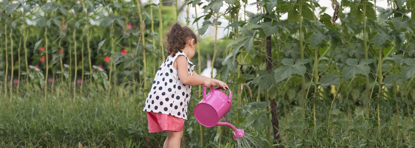 a little girl waters flowers with a large pink watering can