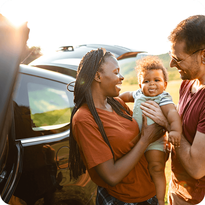 Smiling family with baby near car at sunset, representing Guardian Credit Union’s Insurance Services for family protection
