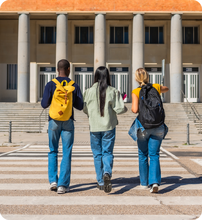 Three students crossing the road to a College Building on campus