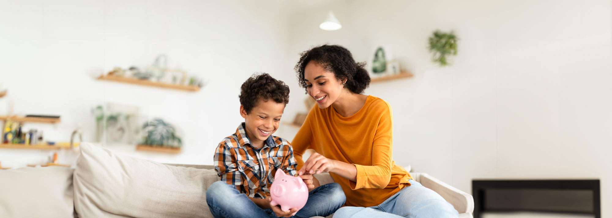 A mother helps her son learn about savings and puts money in a piggy bank.