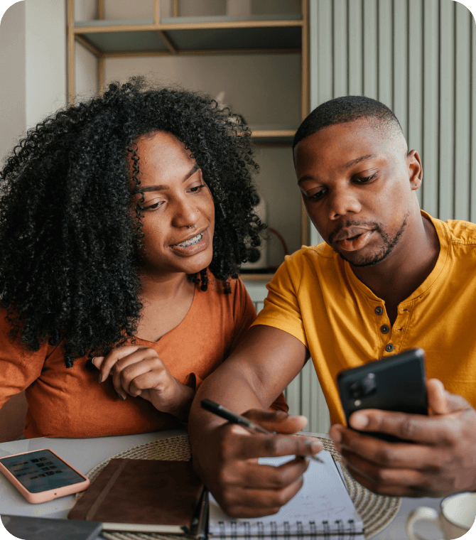 Young couple reviews budget on phone while taking notes, planning with Guardian Credit Union tools