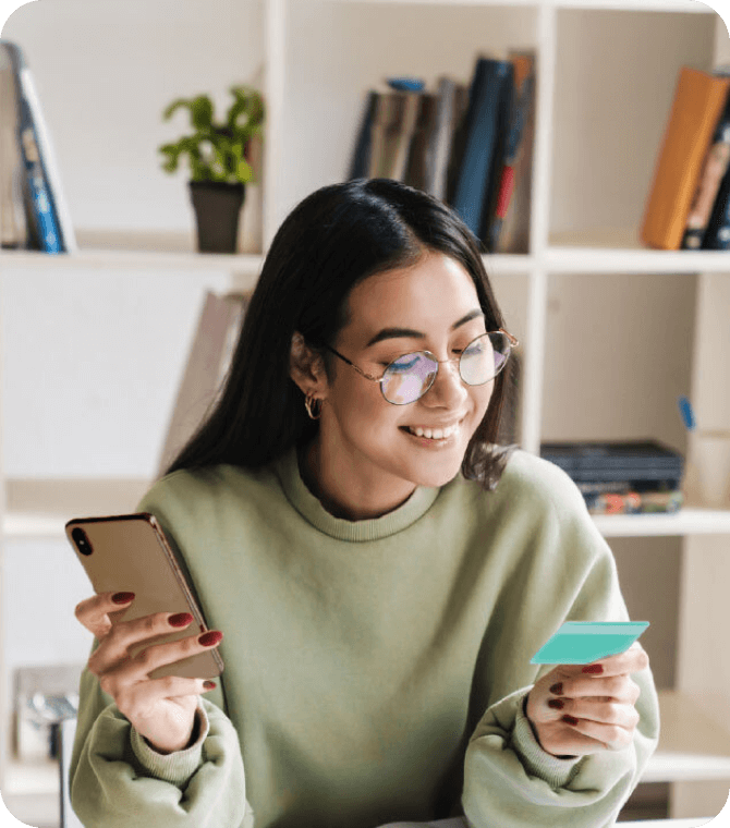 Teen  holding smartphone and Greenlight debit card, managing money through Guardian CU youth checking tools