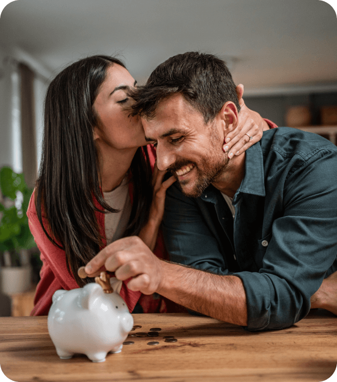 Smiling couple saving coins in piggy bank, representing Guardian Credit Union checking and savings