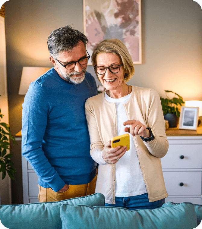 Smiling couple standing in living room using smartphone together, representing online banking confidence