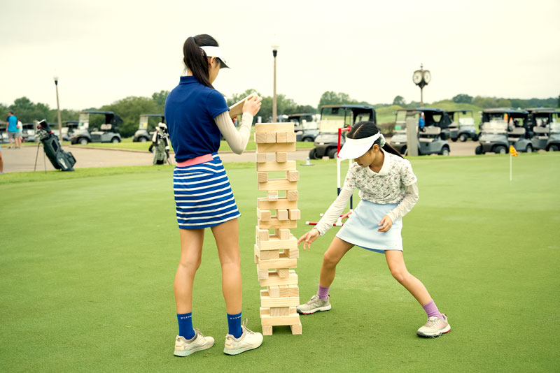 Two girls are playing Giant Jinga outside on the grass.