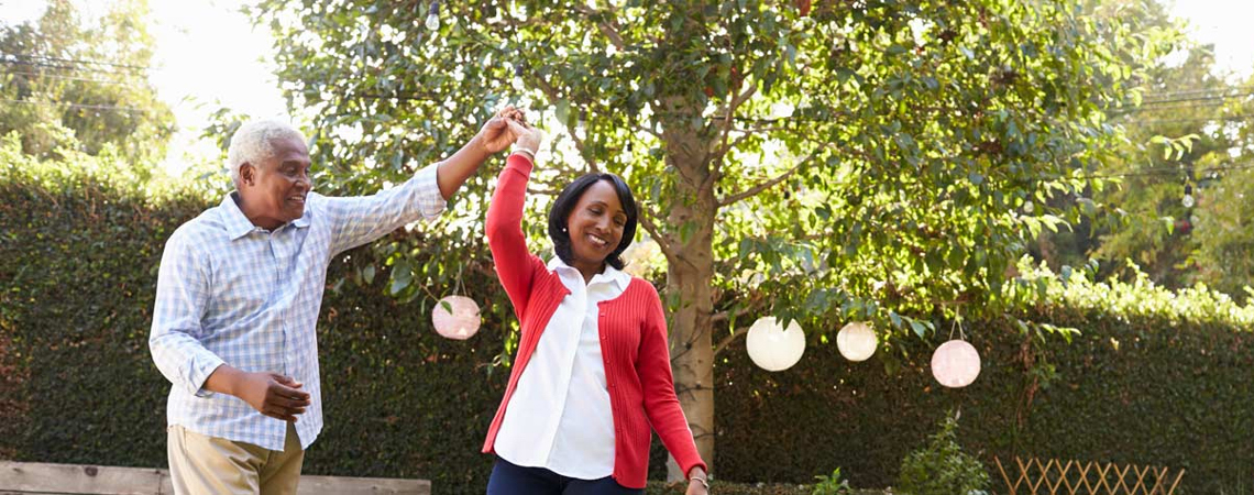 Smiling retired couple dancing in their backyard, relieved to be free from financial worries.