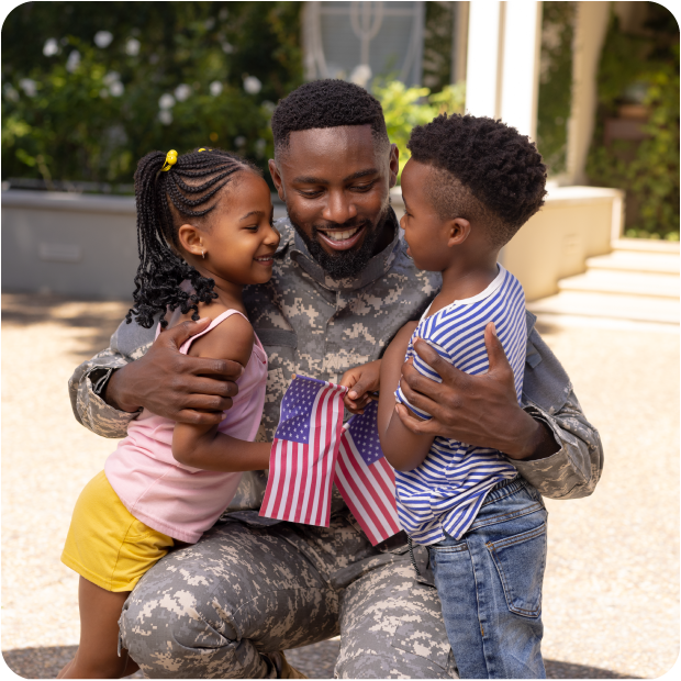 Veteran soldier hugging his young children, a boy and a girl while they are holding american flags.